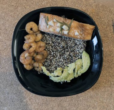 Izgara somon, karides ve mantar masasındaki siyah tabakta susam tohumlu avokado..