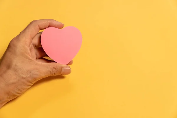 stock image Pink heart paper in hand on yellow background