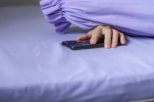 A black smartphone in man hand on purple bed