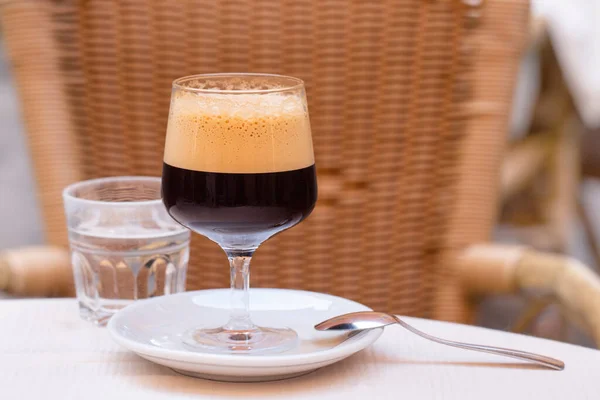 背の高いワイングラスでカフェShakerato 屋外のイタリアのカフェで 冷たいコーヒーは 氷でシェイカーで作られた泡で揺れました 背景にラタン椅子 — ストック写真