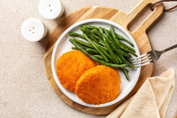 Kızarmış Cordon Bleu 'nun üst görüntüsü erimiş peynir ve jambonlu, ekmek kırıntılı, yeşil fasulyeli. Yukarıda, en üstte, sebzeli pirzola..