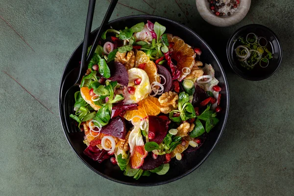 Winter salad with beetroot, oranges, walnuts, pomegranate, dried cranberries, valerian lettuce,  iceberg, onion and blue cheese. Healthy eating. Honey and olive oil dresseng. Above,green background.