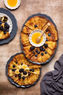 Breakfast with thin Crepes, banana, honey and berries Top view, brawn background. Homemade thin pancakes or crepe.