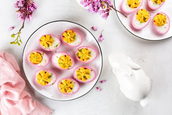 Stock image Stuffed Pink Deviled Eggs with  pepper and mayonnaise colored with beetroot. Easter food concept, spring flowers, easter bunny. Top view.