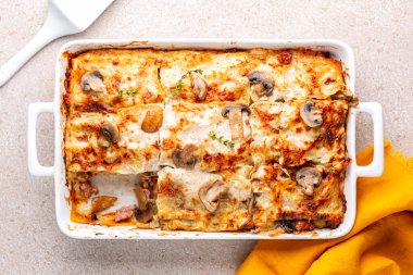 Top view of homemade white lasagna with porcini and champignon mushrooms, onion and sausages. Pasta in casserole with parmesan cheese and bechamel sauce.