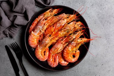 Top view of giant argentinian red prawns, grilled. Black plate. Dark grey background.