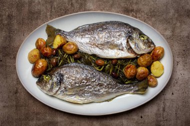 Fırınlanmış yaldızlı başlık, dorada ya da orata balığı olarak da bilinir, uzlaşmalı, zeytinli ve taze patatesli, Akdeniz yemeği, sağlıklı yemek..