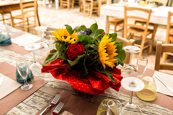 Beautiful summer restaurant dinner table set for an event, party, birthday in the garden, outdoor. Banquet rustic wood table with sunflowers and roses bouquet. Italy.
