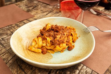 Restoranda İtalyan yemeği. Tagliatelle ragu, geleneksel makarna türü, klasik et soslu yumurta eriştesi veya Bolonez sosu, kahverengi ahşap masa. Kırmızı şarap kadehi. Yaşam tarzı fotoğrafı.. 