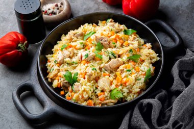 Chicken Pilaf, pilau or biryani. Dish made of long-grain rice, chicken meat and vegetables, onion, carrots, spices and parsley. Eastern cuisine. Dark grey background. clipart