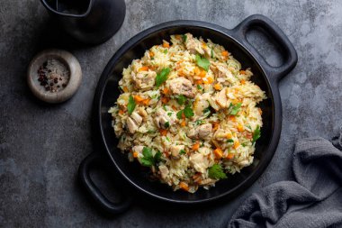 Chicken Pilaf, pilau or biryani. Dish made of long-grain rice, onion, carrots, spices and parsley. Eastern cuisine. Dark background, top view. clipart