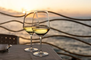 İki kadeh beyaz şarap ve arka planda deniz sahilinde güzel bir günbatımıyla romantik bir akşam. İtalya, Sicilya, akşam, yaz.