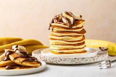 Beyaz masada servis edilen ev yapımı krep, çikolata serpilmiş şurup ve dilimlenmiş muz ile kahvaltı..