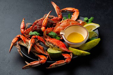 Akdeniz buğulamalı, pişmiş mavi yengeç, limon, zeytinyağı ve limon suyu soslu siyah bir tabak. İtalyan denizine yakalanmış. Karanlık taş arkaplan.