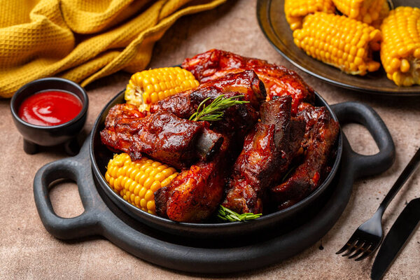 Food board with baked pork ribs with corn cobs, barbecue sauce, rosemary. Brown table background. Meat dinner.