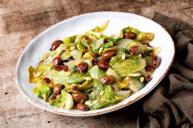 İtalyan salatası sotelenmiş geniş yapraklı hindiba ya da taggiasca zeytinli salata, çam fıstığı, kuru üzüm. Vejetaryen yemeği. Kahverengi tablo yüzeyi.