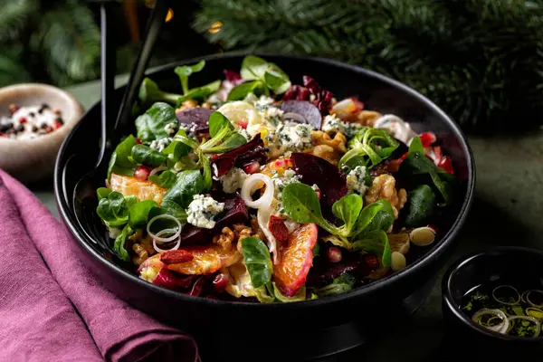 Close up of Christmas winter salad with beetroot, oranges, walnuts, pomegranate, dried cranberries, lettuce, blue cheese. Pink wine in glass. Honey and olive oil dressing.