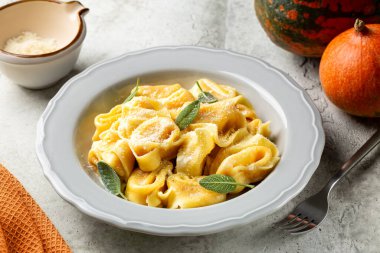 İtalyan cappellacci, tortelloni, tortelli veya ravioli ile doldurulmuş kabak, parmesan peyniri, hindistan cevizi ve adaçayı. Tam balkabağı ve arka planda sert peynir.. 