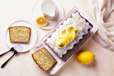 Ev yapımı kahvaltı manzarası. Limon aromalı dilimlenmiş kek, şeker ve limon, beyaz tabakta haşhaş tohumu ve açık arkaplan.