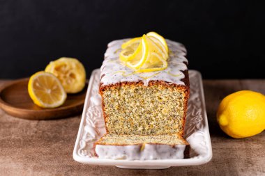 Sliced pound cake made with lemon zest, sugar and lemon glaze and poppy seeds on a brown table and black background.  clipart