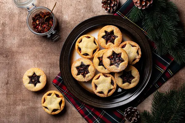 Traditional british christmas Mince pies on a brown plate, sprinkled with sugar. Also called mincemeat or fruit pie, filled with a mixture of fruit, spices and suet. Festive table, directly above.
