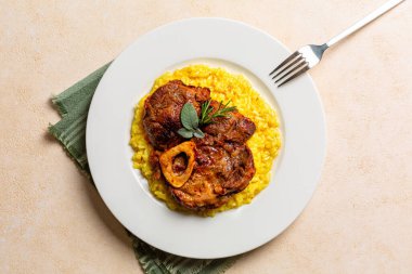 İtalyan yemeği Ossobuco 'nun üst tabağı, safran risotto alla milano ile servis edilen kemikli haşlanmış sığır eti, Lombard mutfağı spesiyali. Bej arkaplan.