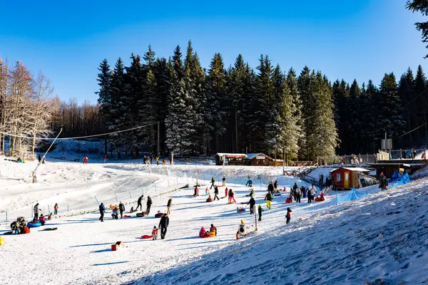 Family winter ski resort Il Lago della Ninfa. Monte Cimone, mountains in the northern Apennines, of Italy, Emilia-Romagna. Slope for children sleighing, snow tubing. People figures, silhouettes, no visible faces.