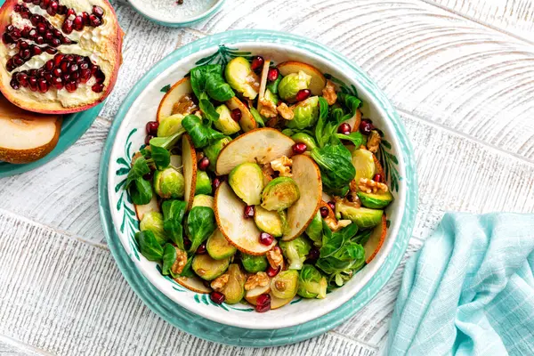 Winter salad with roasted brussel sprouts,  pear, walnut, pomegranate, valerian salad leaves with olive oil, mustard and balsamic vinegar. Flat lay.