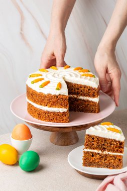 Cevizli ev yapımı havuçlu kek, krem peynirli buzlu. Renkli Paskalya yumurtaları. Kadın elleri tatlı servisi yapıyor. Neşeli arkaplan.