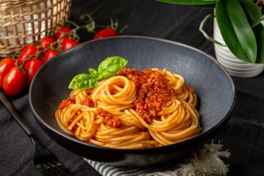 Vejetaryen bolonez soslu, soya, domates ve sebzeli siyah bir tabak spagetti ile akşam yemeği. Vejetaryen makarna. Koyu renkli tablo tekstili.