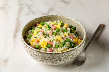 Kanton usulü kızarmış pirinç ve yumurta, yeşil bezelye, jambonlu biftek, taze soğan, bej bir kasede uzun pirinç, beyaz mermer bir masada çatalla servis edilir. Avrasya mutfağı.