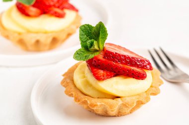 Vanilyalı kremalı çilekli turtalar. Kremalı, vanilyalı ve kurabiye hamurlu mini meyveli tartlar. Tatlı. Beyaz tabak.