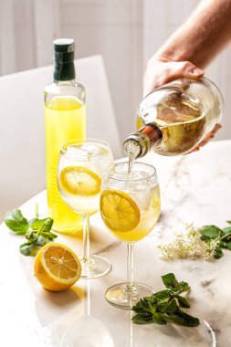 Limoncello Spritz kokteyli, limoncello karışımı, limonata, buzlu soda ve limonata. Mans bir şişe tutuyor, beyaz şarap akıyor. İtalyan yaz içeceği. 