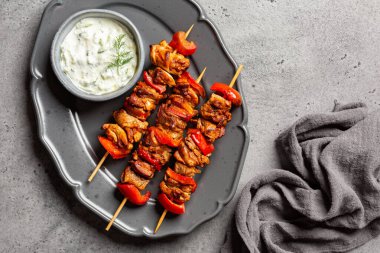 Akdeniz usulü ızgara tavuk şişi, marine edilmiş tavuk ve kırmızı dolmalık biberle yapılmış. Yoğurt, rendelenmiş salatalık, limon suyu ve zeytinyağından yapılmış Yunan Tzatziki sosu. Peçeteli gri masa yüzeyi