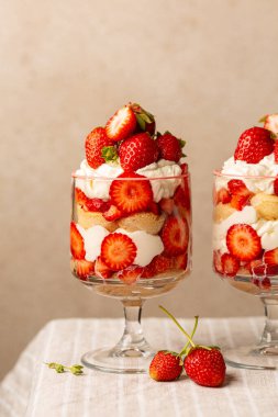 Çilekli tiramisu ya da iki bardakta ıvır zıvır. Işık masasında İtalyan tatlısı ve bej arka plan. Dikey resim.