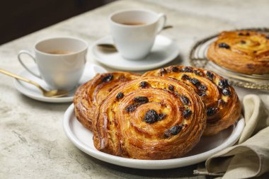 Fransız kahveli ya da espresso kahveli ve kruvasanlı bir masa. Acı kuru üzüm, salyangoz ya da ağrı russe olarak da bilinir, kremalı ve kuru üzümlü bir sarmal hamur işidir..
