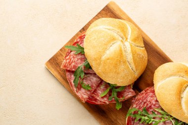 Sandviç ya da panino dilimlenmiş salam, sosis, domates, roket ya da roka ile ahşap bir tahta üzerinde bej masa..