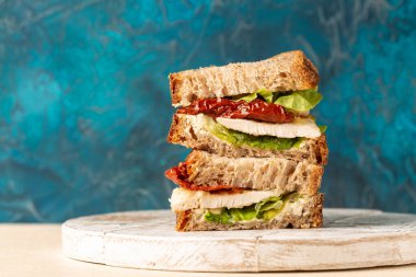 Buğday ekmeği, ricotta peyniri, marul ve kurutulmuş domatesli tavuk göğsü sandviçi. Mavi arkaplanda, boşluğu kopyala.