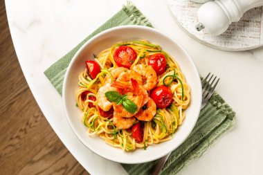 İtalyan yaz deniz ürünleri makarnası. Karides, domates ve kabak ya da kabak, mermer bir masada beyaz bir tabakta spagetti..