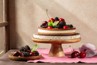 Taze meyve, kiraz, böğürtlen ve kırsal bir masada naneli çikolatalı peynirli kek. Yaz güneşi ışığı. Bej arkaplan. 