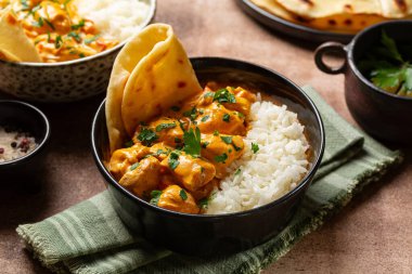 Uzun pirinçli tavuk körisi ve siyah kasede naan ekmeği. Kahverengi tablo arkaplanı.