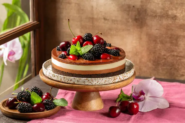 Pişirilmemiş yaz çifte çikolatalı cheesecake taze meyve, kiraz, böğürtlen, nane. Kahverengi kırsal masa, pencere. 