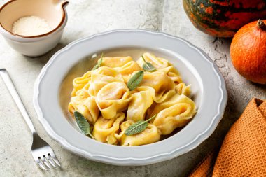 İtalyan cappellacci, tortelloni, tortelli ya da ravioli, balkabağı, parmesan peyniri, hindistan cevizi ve adaçayı ile doldurulmuş. Arka planda tam kabak ve peynir. Açık gri doku tablosu. 