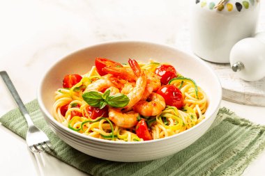 İtalyan yaz deniz ürünleri makarnasından yakın çekim. Karides, domates ve kabak ya da kabak, mermer bir masada beyaz bir tabakta spagetti..