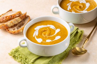 Vegan curried pumpkin lentil soup with vegetable cream and fresh whole grain bread. Healthy homemade dinner. Beige table background. clipart