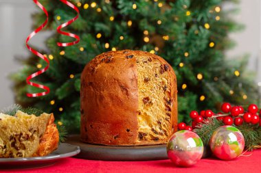 İtalyan Noel 'i ve Yeni Yıl pastası Panettone kırmızı masa örtüsü ile şenlik masasında. Aslen Milan 'dan gelen üzümlü tatlı ekmek, Noel ağacı ve arka planda ışıklar.