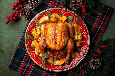 Noel veya Yeni Yıl ziyafeti masası, elma ve portakalla doldurulmuş kızarmış tavuk ve fırında patates, adaçayı ve biberiye ile güzel bir kırmızı tabakta servis ediliyor. Firavun ve süsleme.