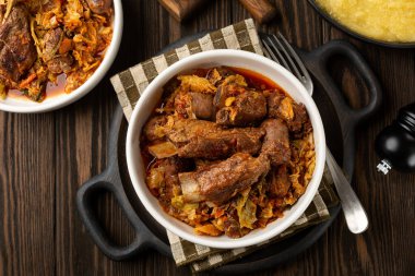 Top view of cassoeula is a typical winter dish popular in western Lombardy, Milanese, North Italian dish. Main ingredients are Savoy cabbage, pork ribs, italian sausage. Polenta. Dark wooden table clipart