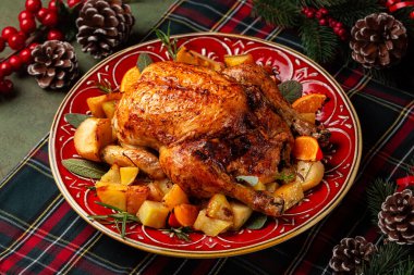 Noel ya da yeni yıl ziyafeti, elma ve portakalla doldurulmuş kızarmış tavuk ve fırında patates, adaçayı ve biberiye ile birlikte yeşil ve kırmızı bir tartan peçetesinde servis edilen güzel kırmızı tabakta..