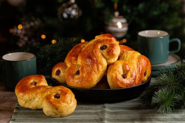 Christmas table with homemade  swedish St Lucia saffron buns.  Coffe or tea cups. Also called  lussekatt or lussebulle, Cornish tea treat bun or revel bun, is a spiced yeast-leavened sweet bun flavoured with saffron and contains dried  raisins.  clipart